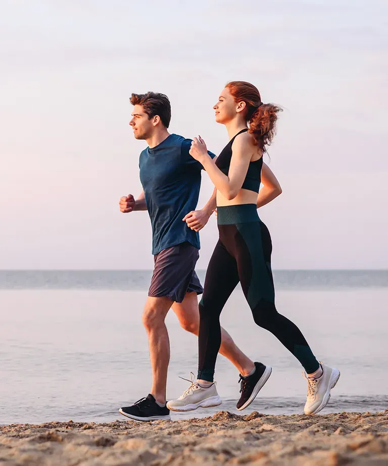 Man and woman jogging together on the beach, staying active with healthy feet and ankles