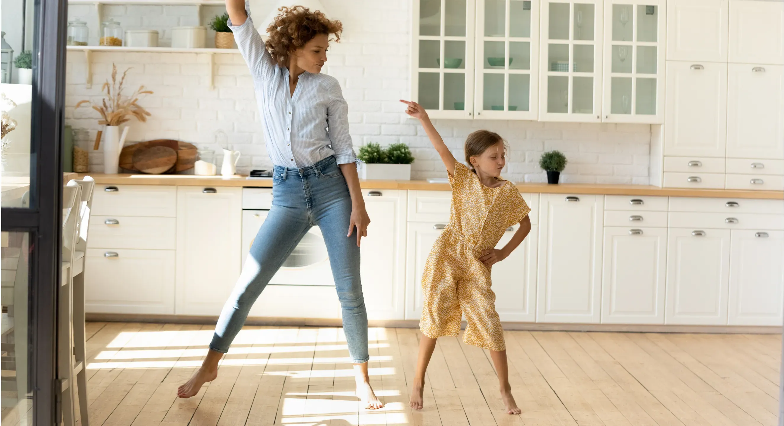 Mother and daughter dancing barefoot together in their kitchen, full of energy and confidence